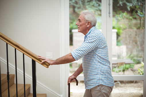 Senior man climbing upstairs with walking stick at home