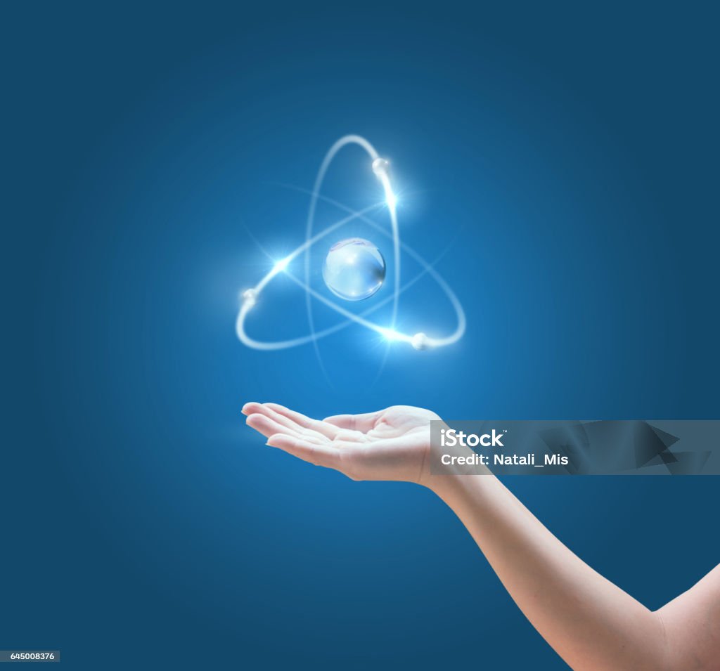 Mano con la imagen del átomo sobre fondo azul. - Foto de stock de Átomo libre de derechos