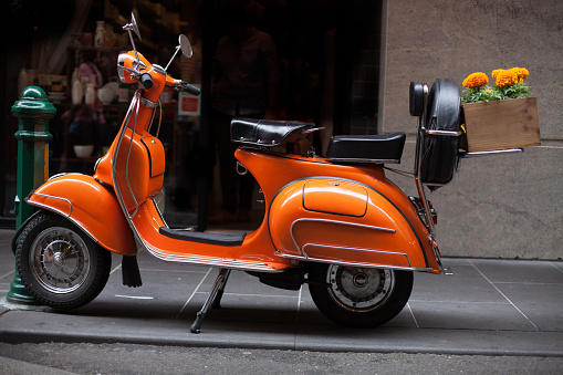 An Orange Scooter with Orange Marigolds in Wooden box on board, parked in a Melbourne Street.
