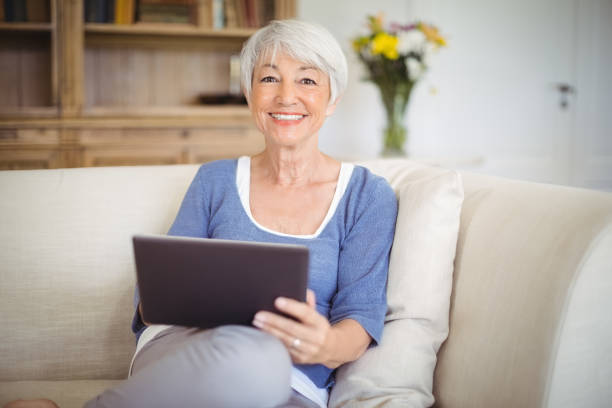 istock Smiling senior woman using digital tablet in living room 645012270