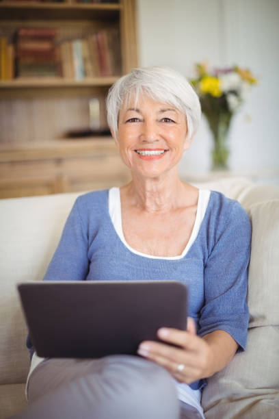 istock Smiling senior woman using digital tablet in living room 645012278