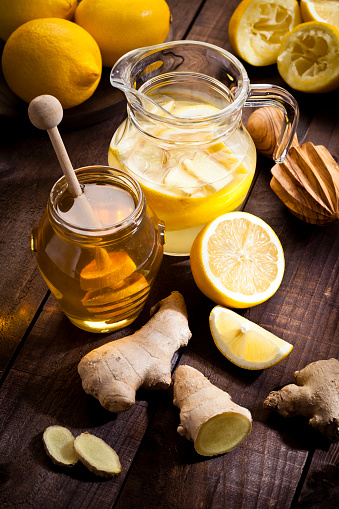 Healthy lifestyle concept, Detox: vertical high angle view of a glass jug filled with lemon infused water, ginger and honey on a rustic wood table. A honey jar is beside the jug and some lemons and ginger pieces completes the composition. Predominant colors are yellow and brown. DSRL studio photo taken with Canon EOS 5D Mk II and Canon EF 70-200mm f/2.8L IS II USM Telephoto Zoom Lens
