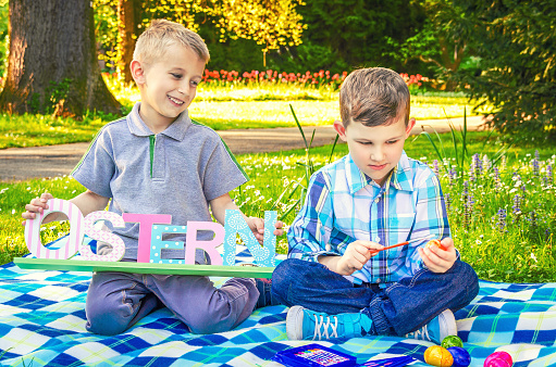 Two little boys children paint Easter eggs and preparing scenery to the Holy Easter holiday in the park. Old Christian and Catholic tradition.