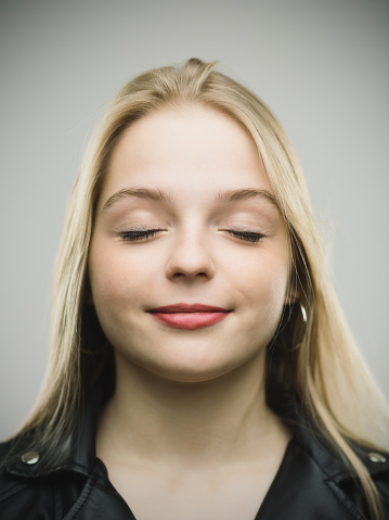 Close-up portrait of happy young woman with beautiful smile and closed eyes. Cheerful female is against gray background. Vertical studio photography from a DSLR camera. Sharp focus on eyes.