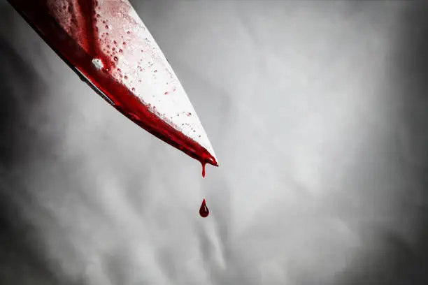 Photo of close-up of man holding knife smeared with blood and still dripping.