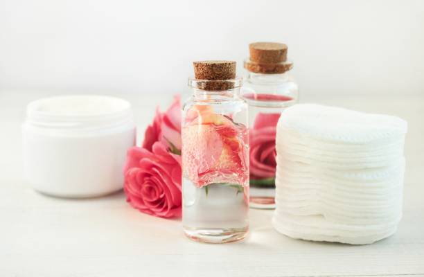 Facial rose extract facial lotion. Glass bottle with attar bubbles and rose petals, cotton pads. Healing homemade skincare moisture toni botanical spa treatment stock pictures, royalty-free photos & images