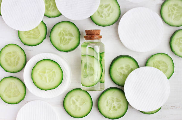 Fresh homemade cucumber facial toner in bottle, green cucumber slices, cotton-pads, top view ingredients. botanical spa treatment stock pictures, royalty-free photos & images