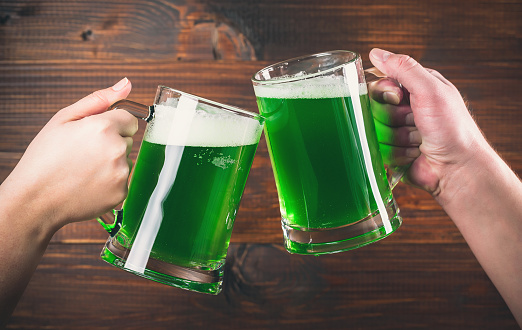 St Patrick's Day concept two mug on hands green beer against wooden background