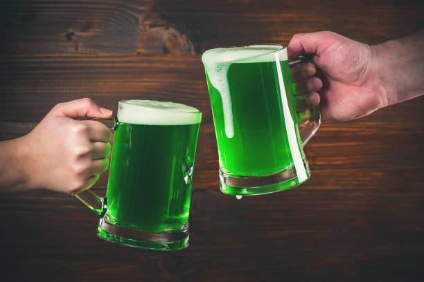 St Patrick's Day concept two mug on hands green beer against wooden background stock photo