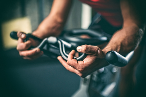 Close up view of male athlete's hands while exercising cycling indoors on stationary bicycle.