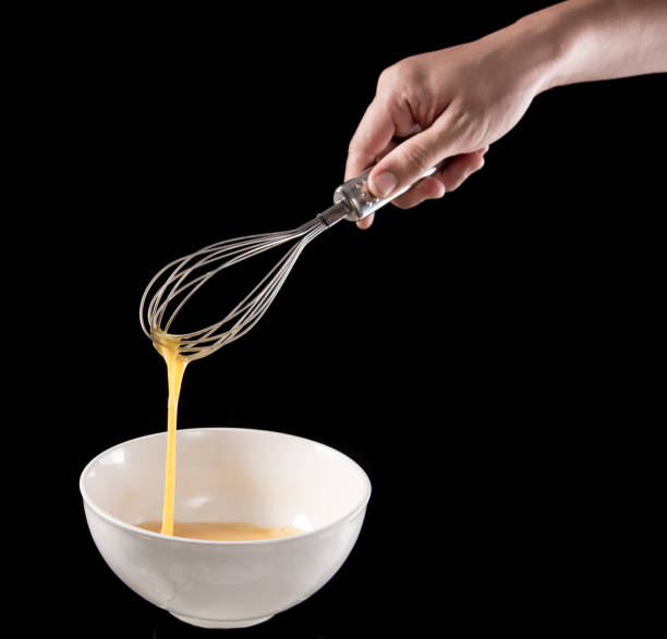 istock Wire whisk with eggs in bowl isolated on black background 645083736