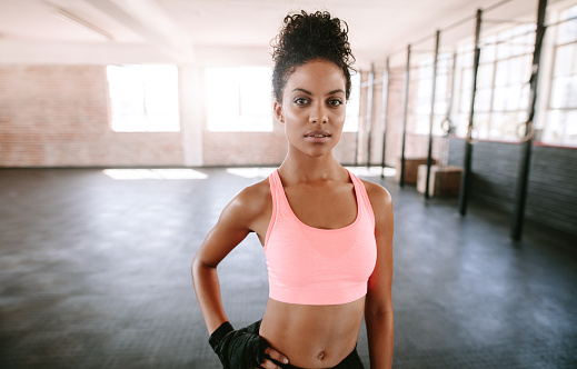 Portrait of fit young woman standing in gym. African female fitness model posing in sportswear.