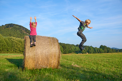 A young children boy and girl (siblings) playing on hay bale summertime. Children summer outdoor activities.