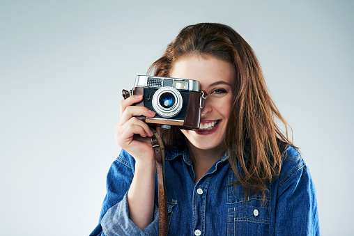 Studio portrait of a young woman using a vintage camera against a grey background