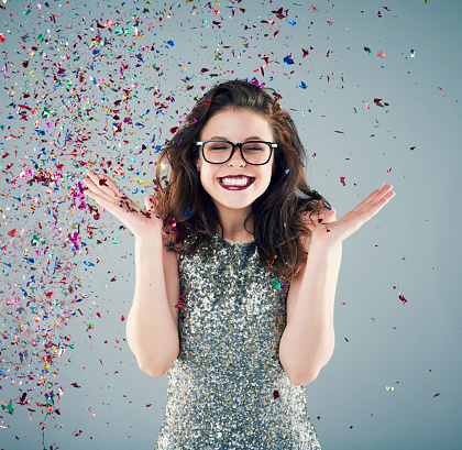 Studio shot of a young woman with confetti falling around her against a grey background