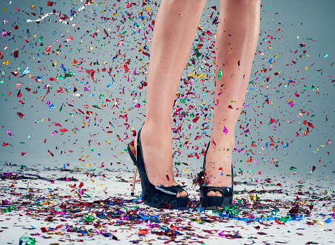 Studio shot of a young woman's legs in a pair of heels with confetti falling around against a grey background