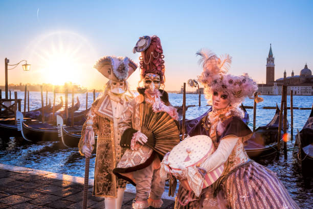 Venice, Italy- February 5, 2016. Venetian costumes pose in front of gondolas during the Venice Carnival days. The most  famous festival in the world. Venetian costumes pose in front of gondolas during the Venice Carnival days. The most  famous festival in the world. gondola traditional boat photos stock pictures, royalty-free photos & images