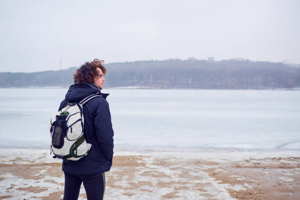 湖でのバックパック冬ジャケットの巻き毛の髪の男旅します。 - landscaped landscape winter usa ストックフォトと画像