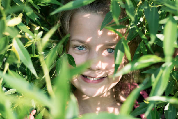 portrait of smiling girl behind many green leaves of willow tree