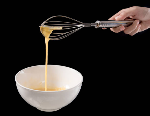 istock Wire whisk with eggs in bowl isolated on black background 645160194