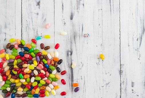 Candy jelly beans of different colors on bright whitewashed wooden background. Space for your text
