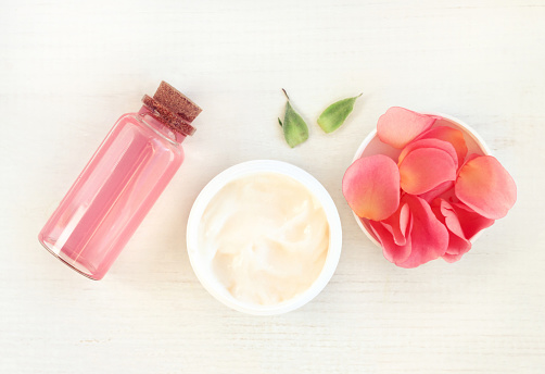 top view. Jar of cream, pink rose petals, facial tonic in bottle.