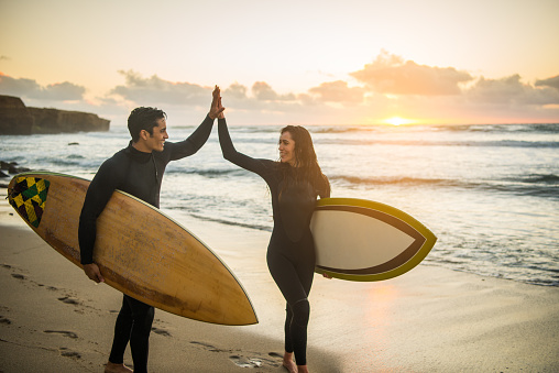 Surfer couple high fiving with their surfboards.
