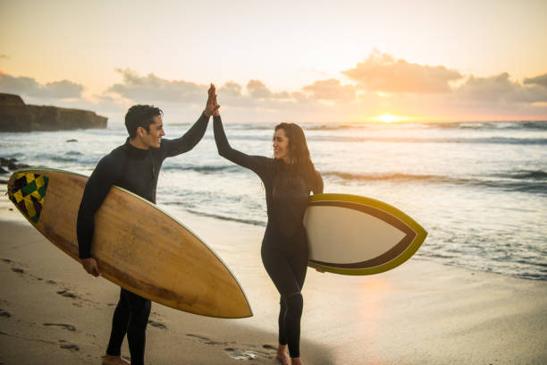 Silhouette of a Couple High Fiving With Their Surboards Surfer couple high fiving with their surfboards. san diego photos stock pictures, royalty-free photos & images