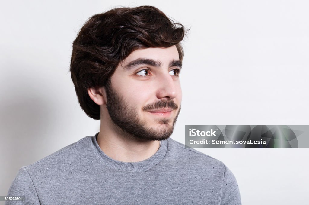 A Closeup Of Stylish Hipster With Trendy Beard And Hairstyle Dark Big Eyes  Dressed In Casual Clothes Looking Happily Aside Portrait Of Handsome Man  With Beard Over White Background Stock Photo -