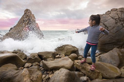 Excited little girl watching waves break on rocky beach