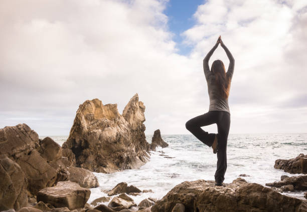 istock Woman doing yoga tree pose and meditating on rocky beach 645234042