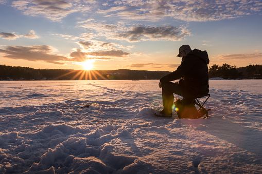 Ice fishing on a lake in Norway at sunset.