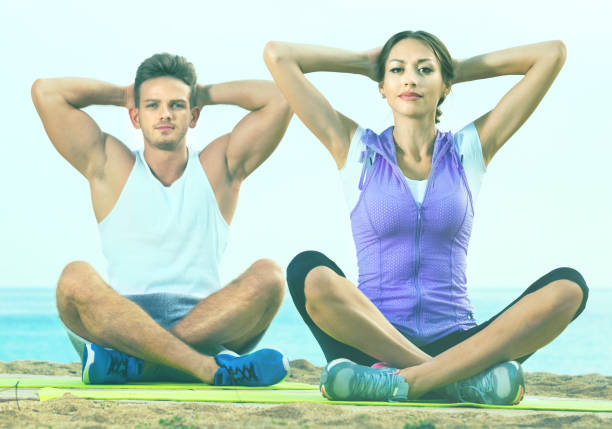 femme et homme assis les jambes croisées font des poses d’yoga sur la plage - men yoga meditating cross legged photos et images de collection