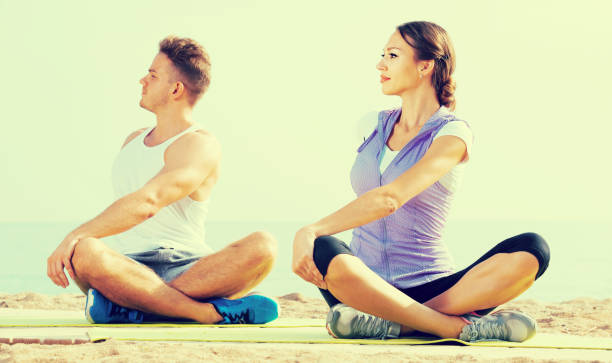jambes croisées couple pratique l’yoga sur la plage de matin - men yoga meditating cross legged photos et images de collection