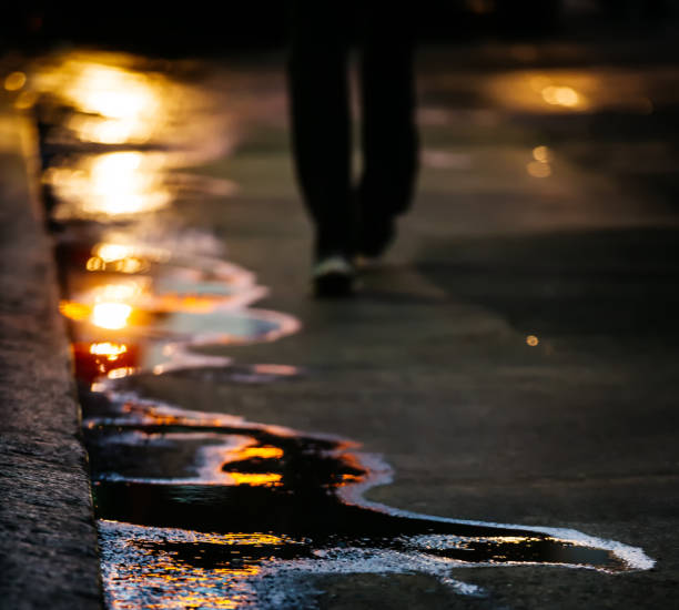 The sun in the puddles. Abstract blurred photography reflection of the evening sun on the asphalt with a silhouette of a man in the background