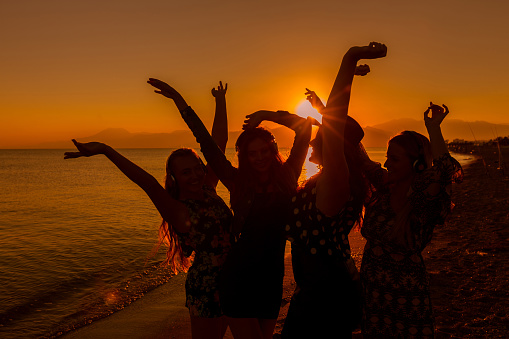 Young women friends dancing on the beach at sunset