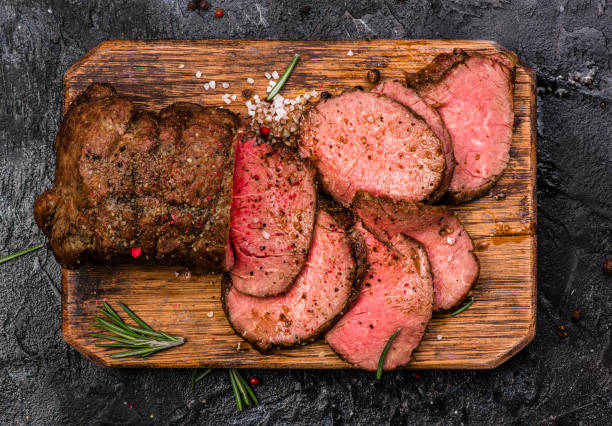 Roast beef on cutting board with salt and pepper. Top view. stock photo