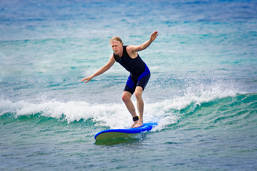 A mature man surfer with an active lifestyle surfing on the beach of Kauai, Hawaii. He is wearing a wetsuit and concentrating on the water sport