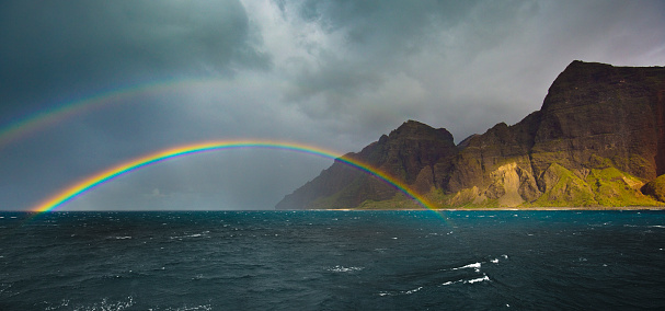 Dramatic double rainbow over the coastal shore of the Na Pali Coast on the island of Kauai, Hawaii. A rugged seashore, a favorite tourist destination on the island.