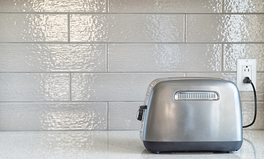 Plugged in retro styled toaster with sliced bread against grey ceramic backsplash in background