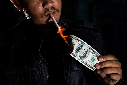 Gangster mafia killer or drug dealer using dollar banknote dirty money received from the illegal business or selling drugs and narcotics lighting his cigarette tobacco., In dark tone.