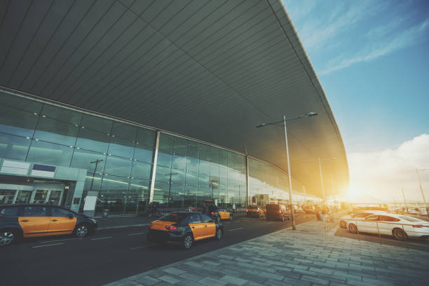 Cabstand in front of modern airport doors in Barcelona, cabrank with a lot of taxis near windowed facade of contemporary Airport terminal in Spain with road, long ceiling and parking lot