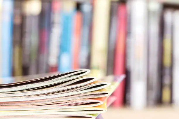 Photo of edge of colorful magazine stacking with  blurry bookshelf