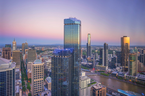 An aerial view of Melbourne cityscape including Yarra River and Victoria Harbour in the distance during sunset with beautiful sun ray bursting through clouds.