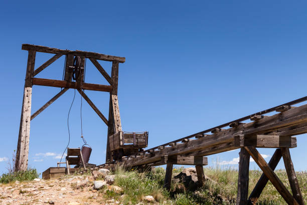 istock Old mining ore cart on trestle with head frame under blue sky. 645356994