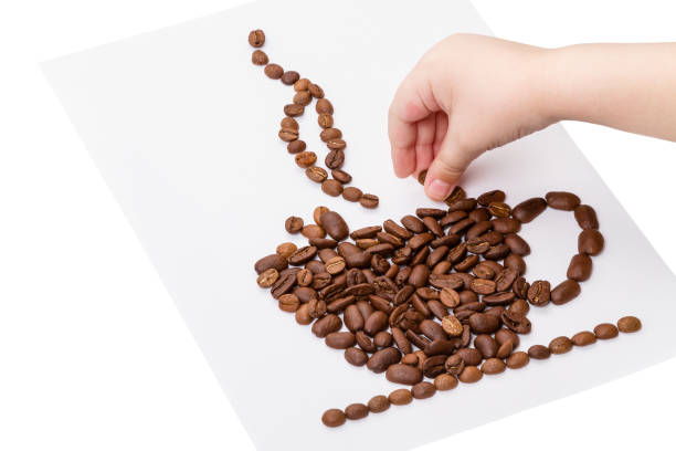 A child collects a cup with a steaming drink made of coffee beans on a white sheet of paper
