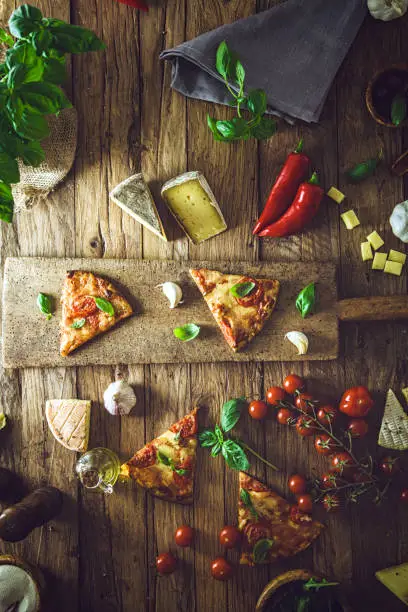 Pizza slice on wood with ingredients. Pizza with cheese, tomatoes and basil. Rustic italian pizza