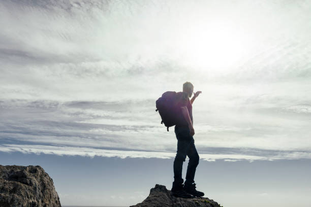 istock man stood on top of rocks backlit in sunflare with backpack. 645377812