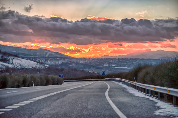 A landscape defined by a red sunset after a snow storm; The main subject is a highway or freeway as seen from the driver's seat