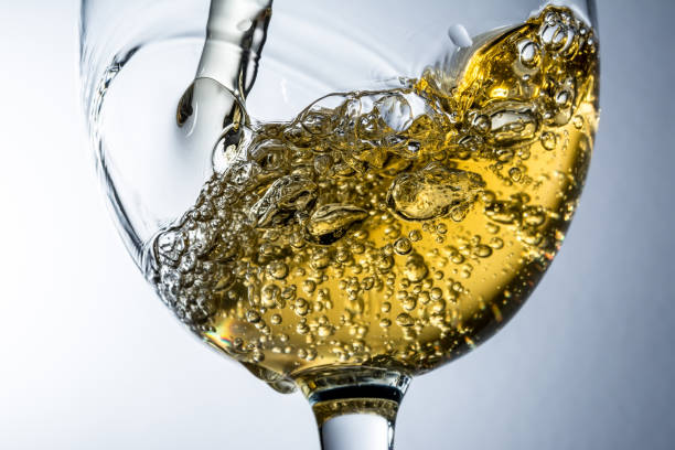 istock Stream of white wine pouring into a glass, white wine splash on grey background 645415718